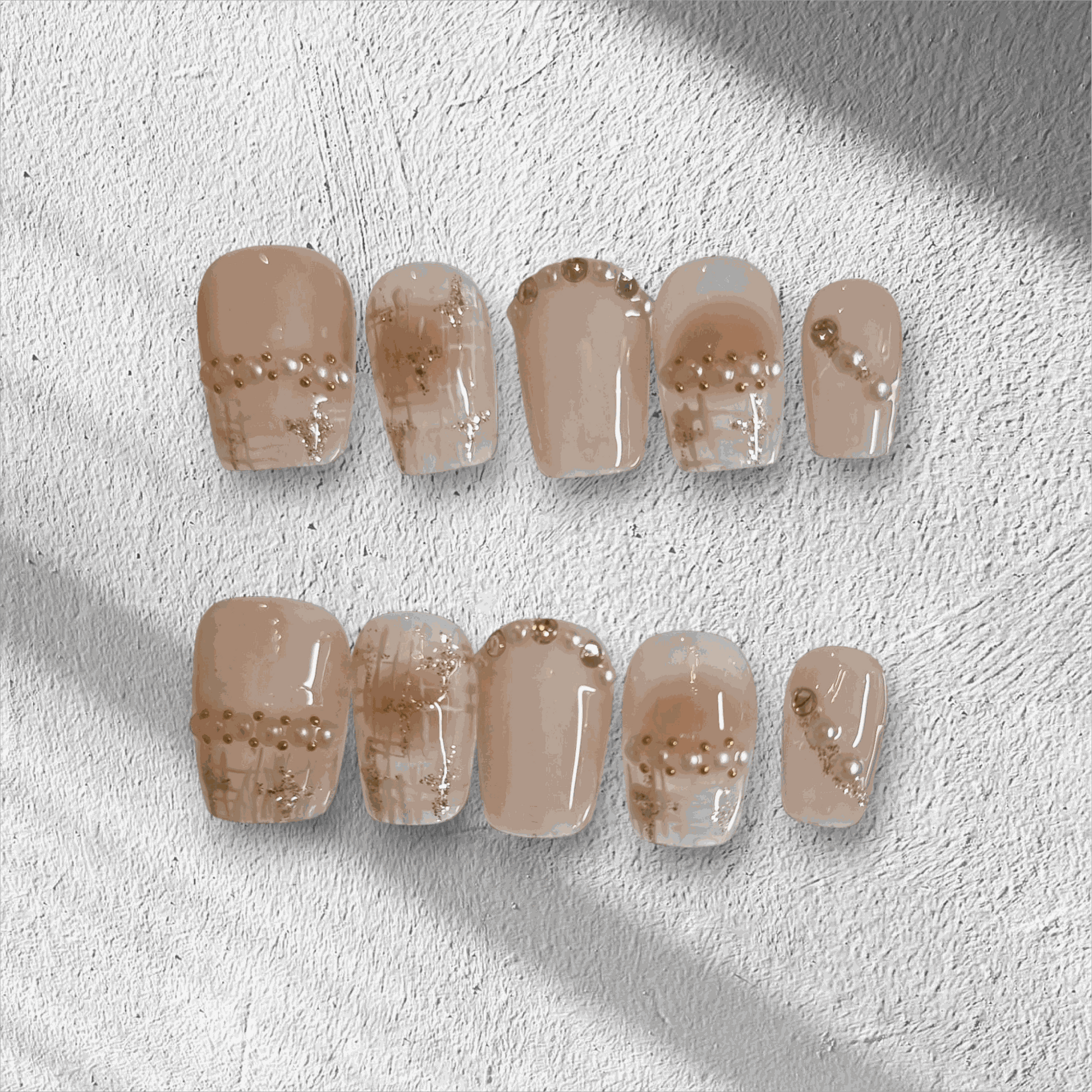 The Corniche Chic press-on nail set in a short square shape, featuring a nude base with delicate pearl and glitter line art details.