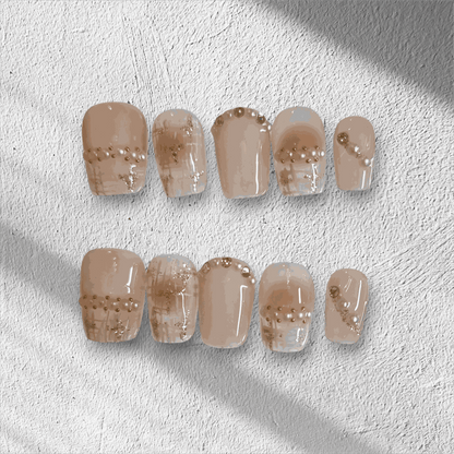 The Corniche Chic press-on nail set in a short square shape, featuring a nude base with delicate pearl and glitter line art details.