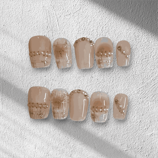 The Corniche Chic press-on nail set in a short square shape, featuring a nude base with delicate pearl and glitter line art details.