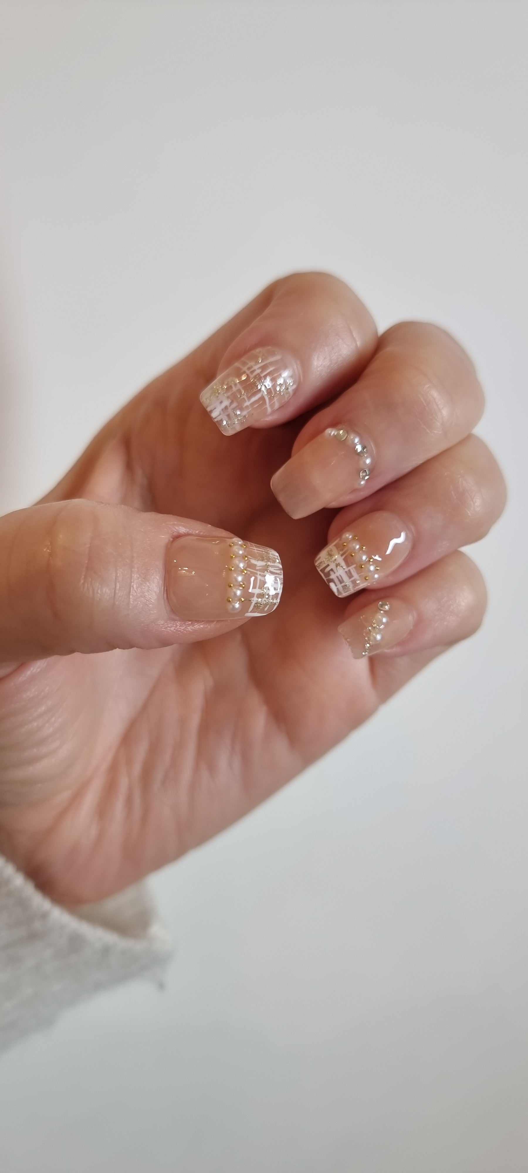 A model's hand wearing the elegant Corniche Chic press-on nails, showcasing the intricate pearl and glitter design.