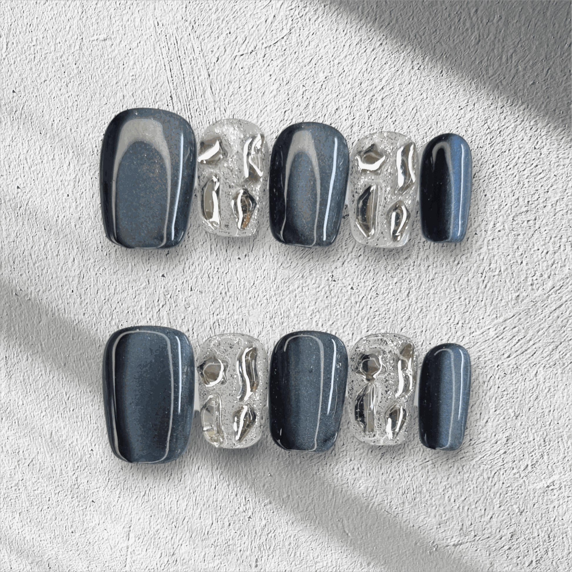 The Days in Dubai press-on nail set in a short square shape, featuring a mix of grey-blue and textured clear nails with molten chrome details.
