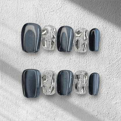 The Days in Dubai press-on nail set in a short square shape, featuring a mix of grey-blue and textured clear nails with molten chrome details.