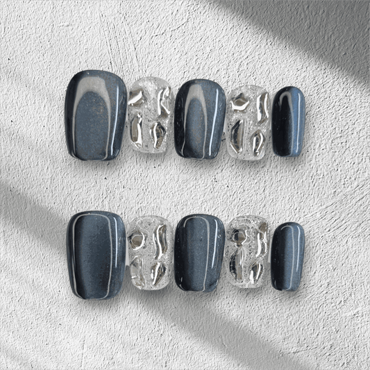 The Days in Dubai press-on nail set in a short square shape, featuring a mix of grey-blue and textured clear nails with molten chrome details.