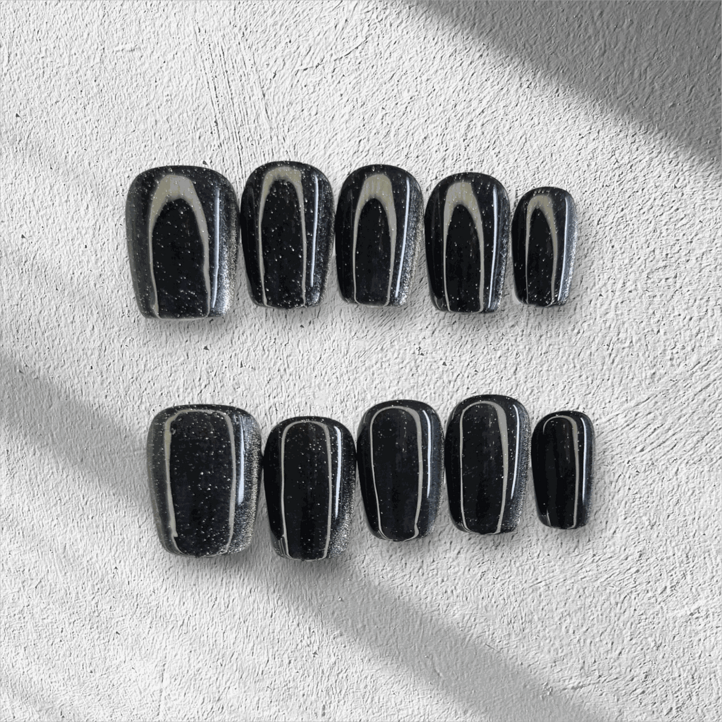 The Deira Dusk press-on nail set in a short square shape, featuring a deep black color with a multi-dimensional glitter finish.