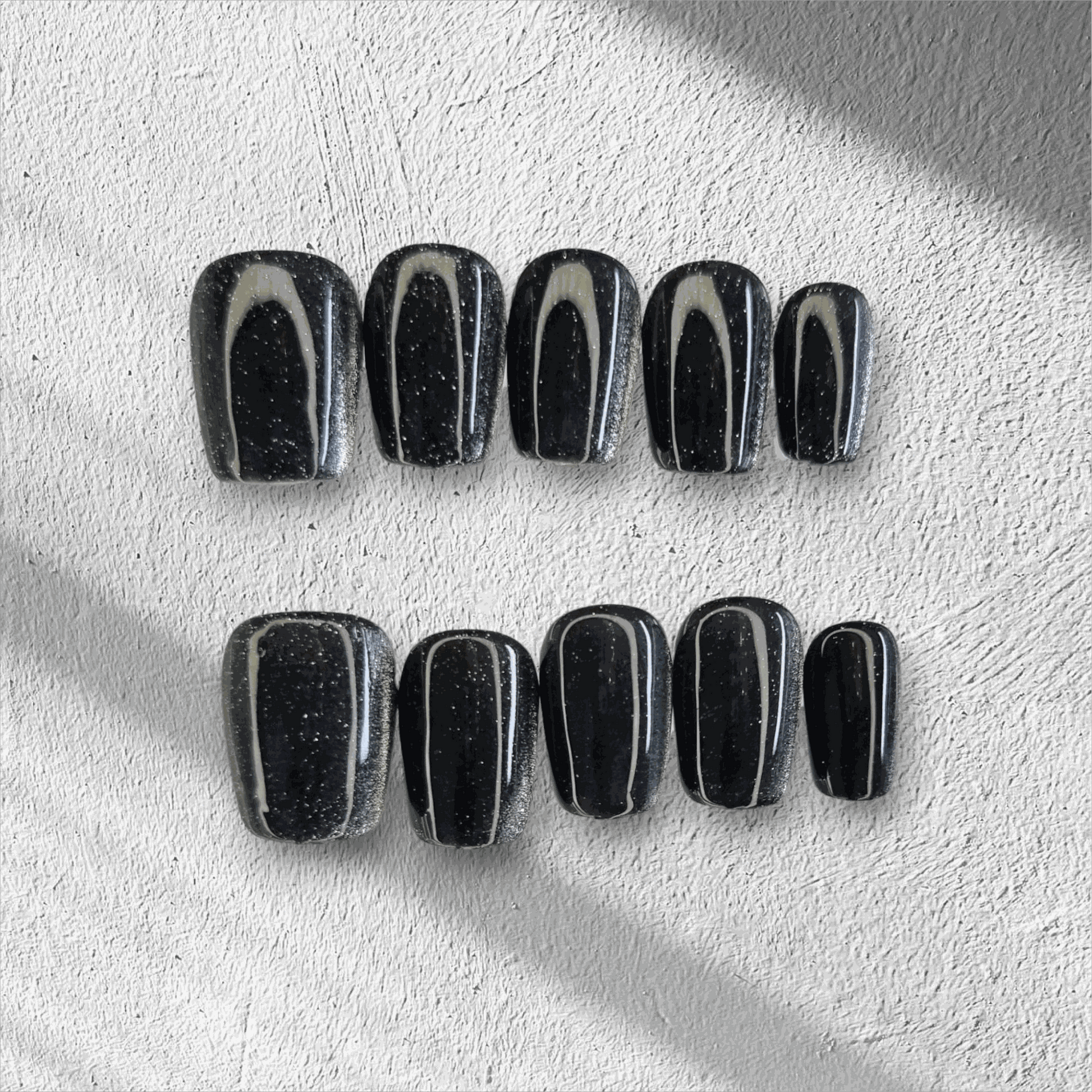 The Deira Dusk press-on nail set in a short square shape, featuring a deep black color with a multi-dimensional glitter finish.