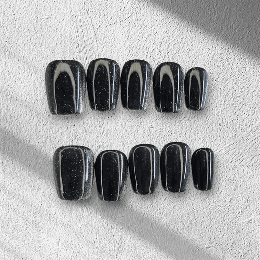 The Deira Dusk press-on nail set in a short square shape, featuring a deep black color with a multi-dimensional glitter finish.