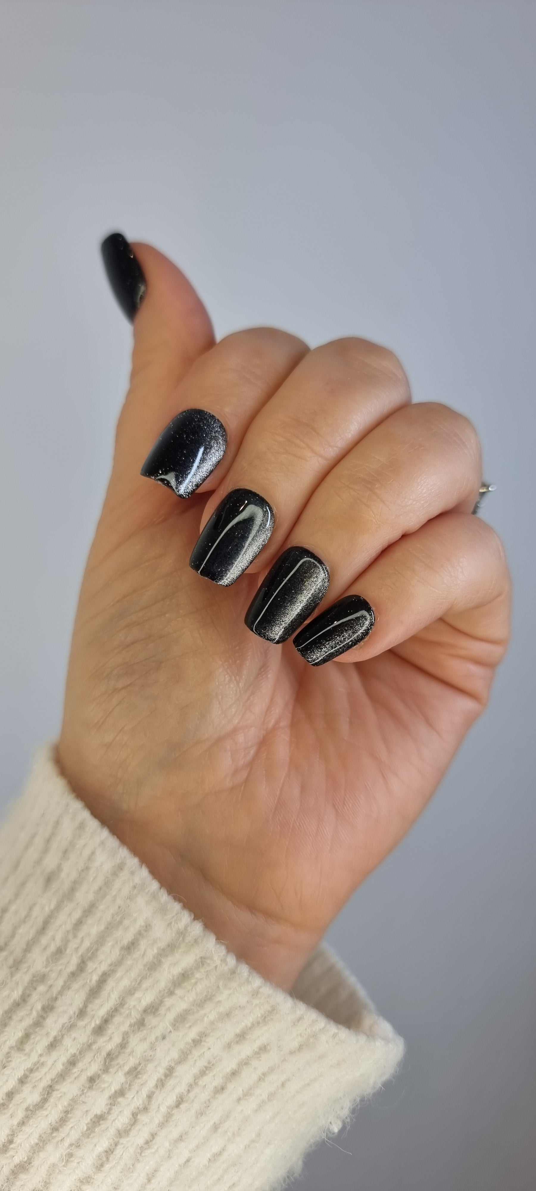 A model's hand wearing the sophisticated Deira Dusk press-on nails, showcasing the sparkling black glitter effect.