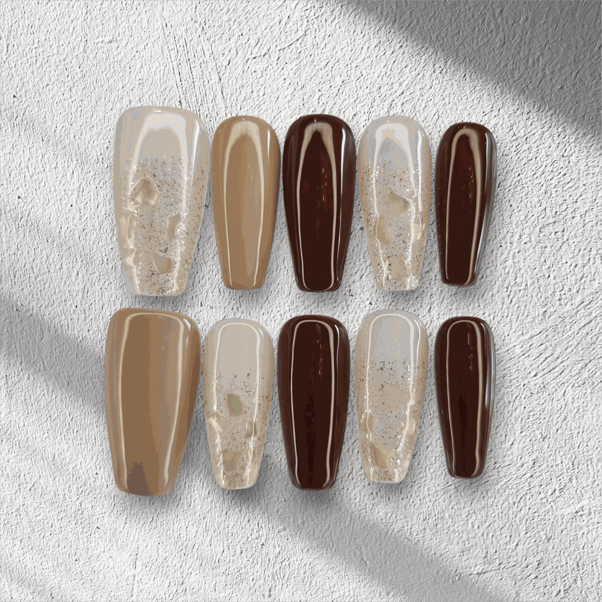 The Desert Crush press-on nail set in a long coffin shape, featuring a mix of brown, nude, and gold glitter nails.