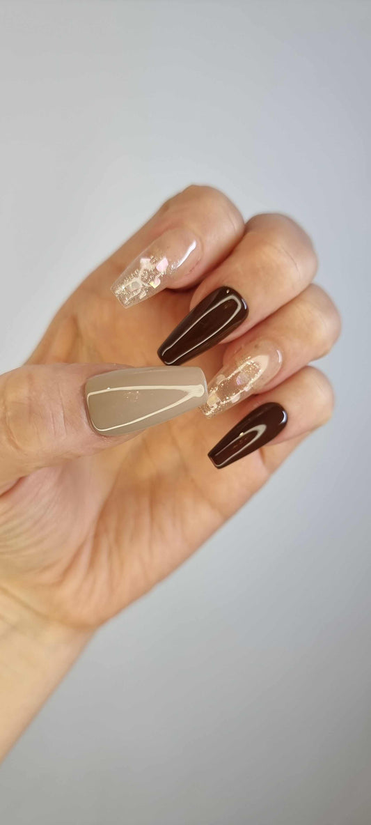 A model's hand wearing the Desert Crush press-on nails, showcasing the elegant mix of brown and gold glitter designs.