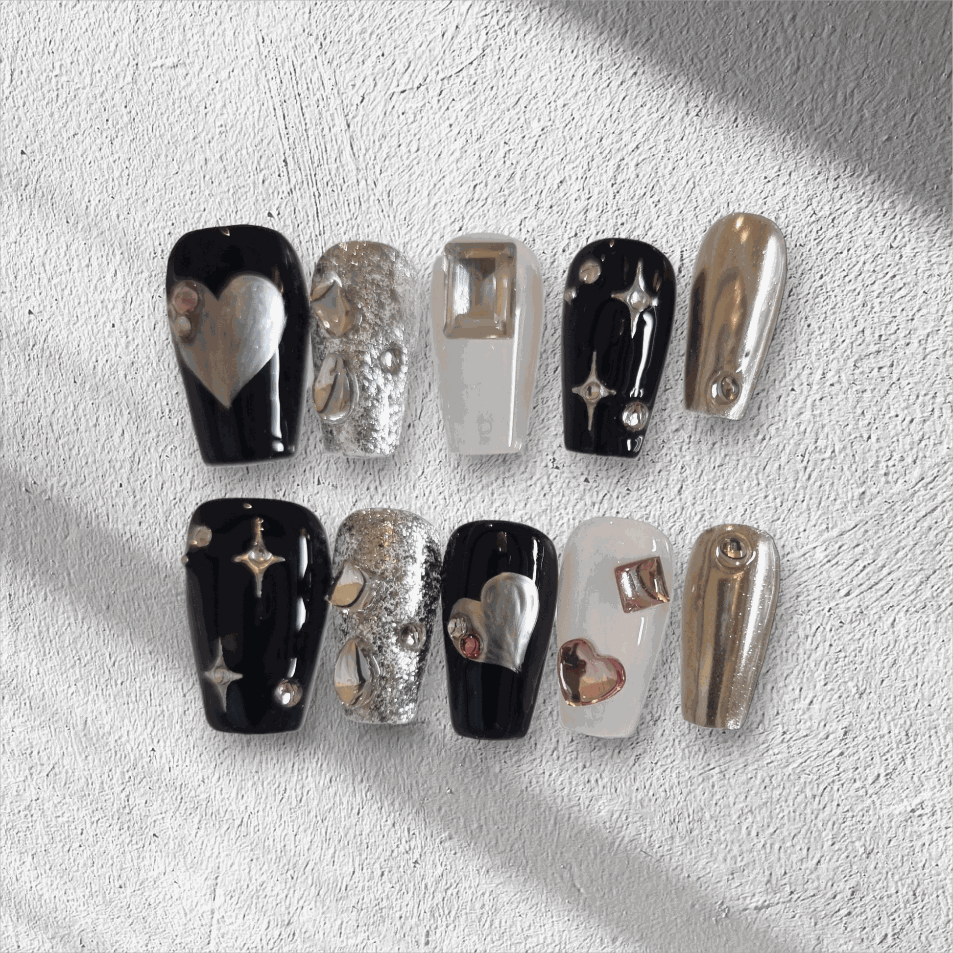 The Doha Dreams press-on nail set in a long coffin shape, featuring a mix of chrome, black, and silver glitter nails with 3D heart and star art.