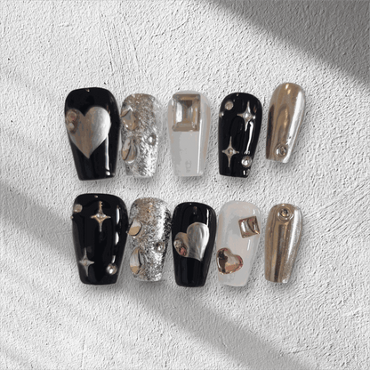 The Doha Dreams press-on nail set in a long coffin shape, featuring a mix of chrome, black, and silver glitter nails with 3D heart and star art.