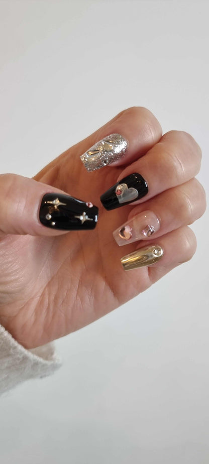 A model's hand showcasing the luxurious Doha Dreams press-on nails, with a focus on the 3D chrome and black nail art.