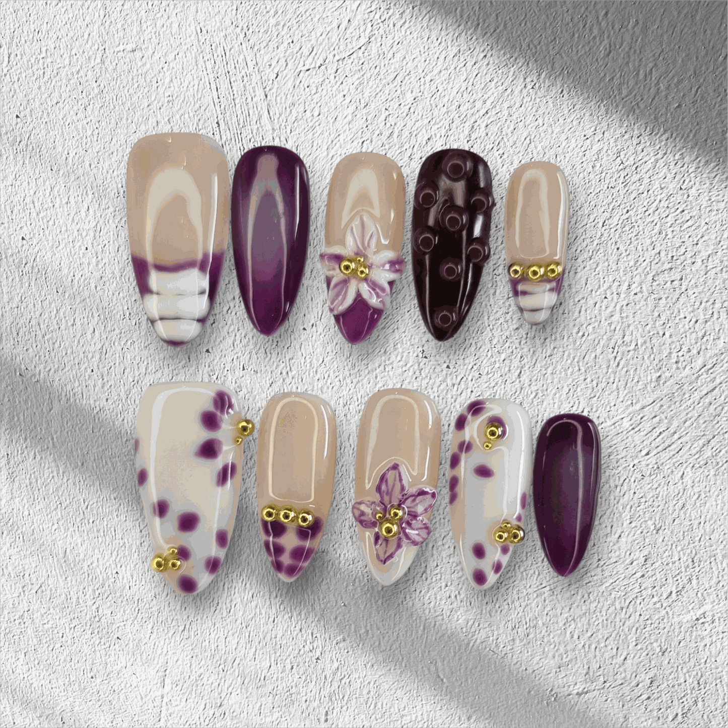 The Emirati Essence press-on nail set in a long almond shape, featuring a mix of purple and nude nails with henna-inspired floral art and gold details.