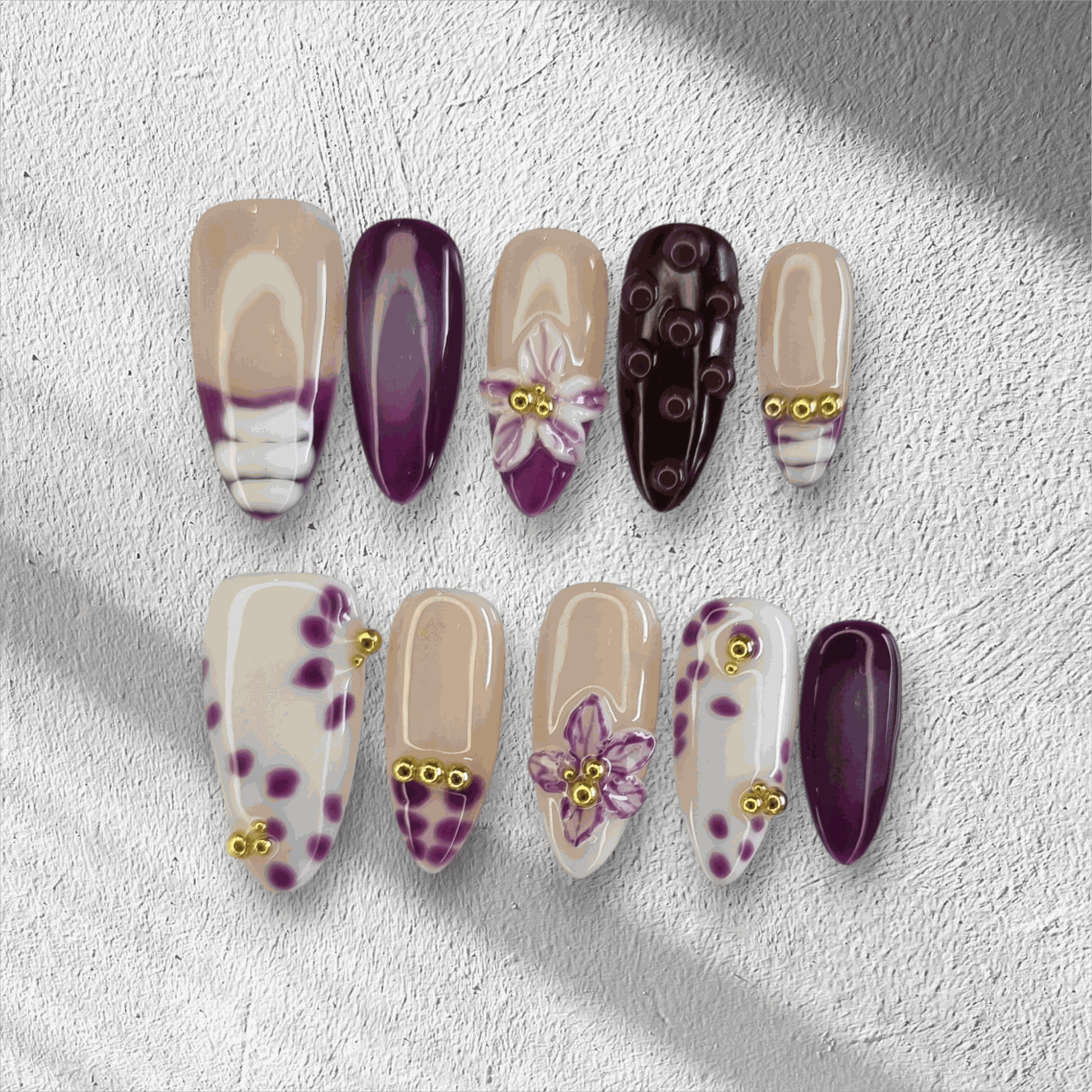 The Emirati Essence press-on nail set in a long almond shape, featuring a mix of purple and nude nails with henna-inspired floral art and gold details.