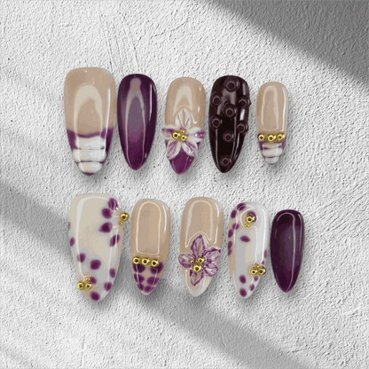 The Emirati Essence press-on nail set in a long almond shape, featuring a mix of purple and nude nails with henna-inspired floral art and gold details.
