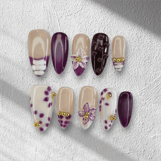 The Emirati Essence press-on nail set in a long almond shape, featuring a mix of purple and nude nails with henna-inspired floral art and gold details.