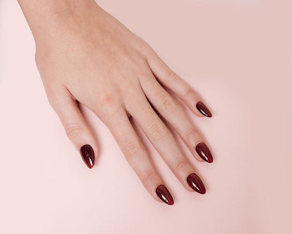 Hand with dark red nail polish on a light pink background