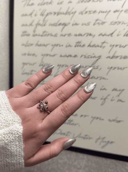 Hand with glittery nails wearing a gold ring with a green gemstone, in front of handwritten text.