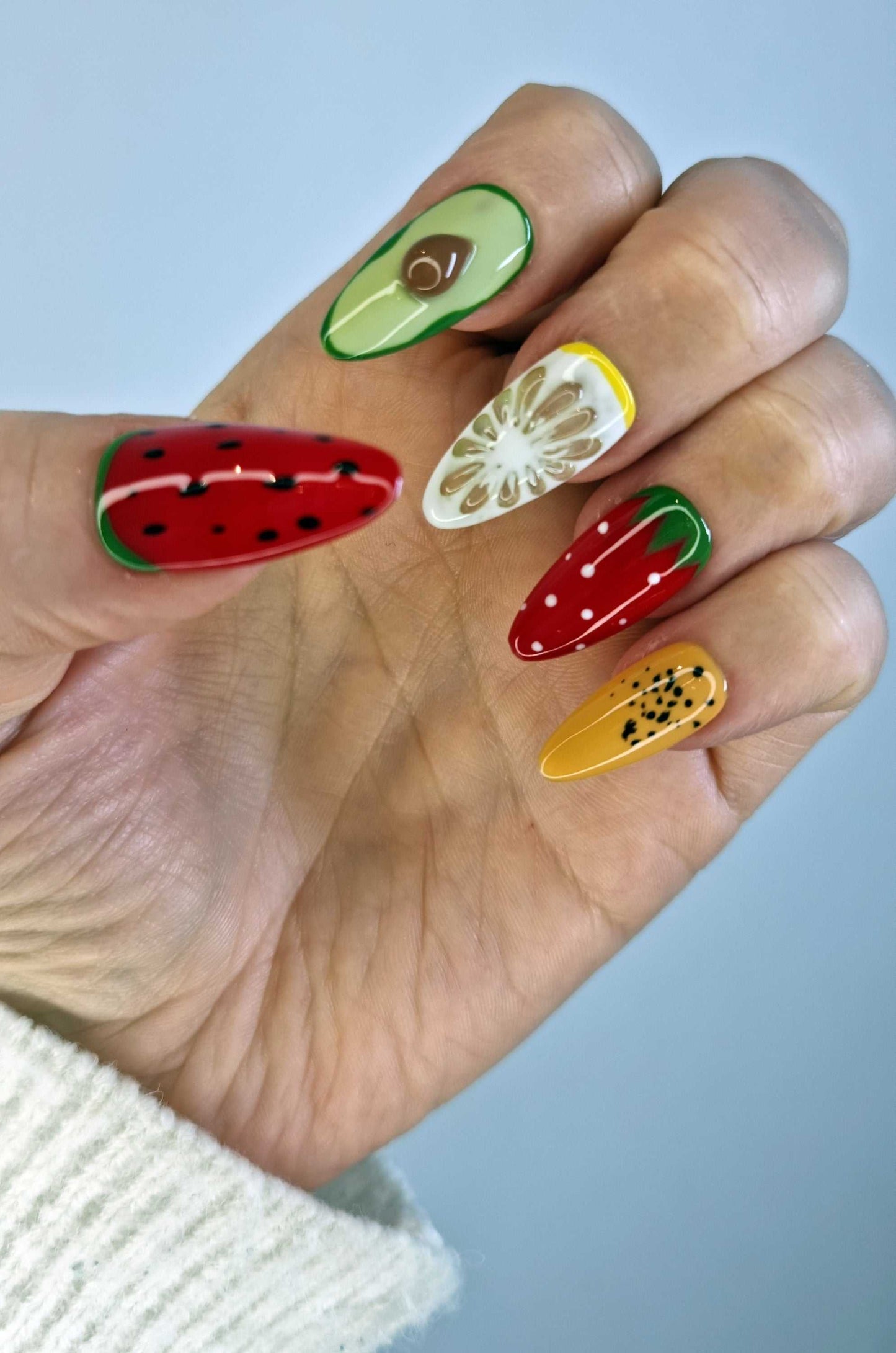 A model's hand showcasing the fun and colorful Fujariah Fruity Flair press-on nails with various fruit art designs.