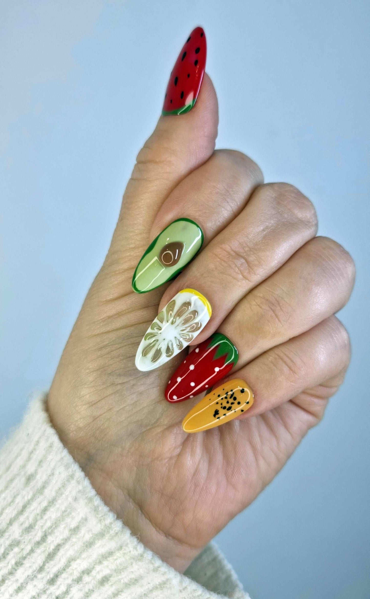 A model's hand showcasing the fun and colorful Fujariah Fruity Flair press-on nails with various fruit art designs.