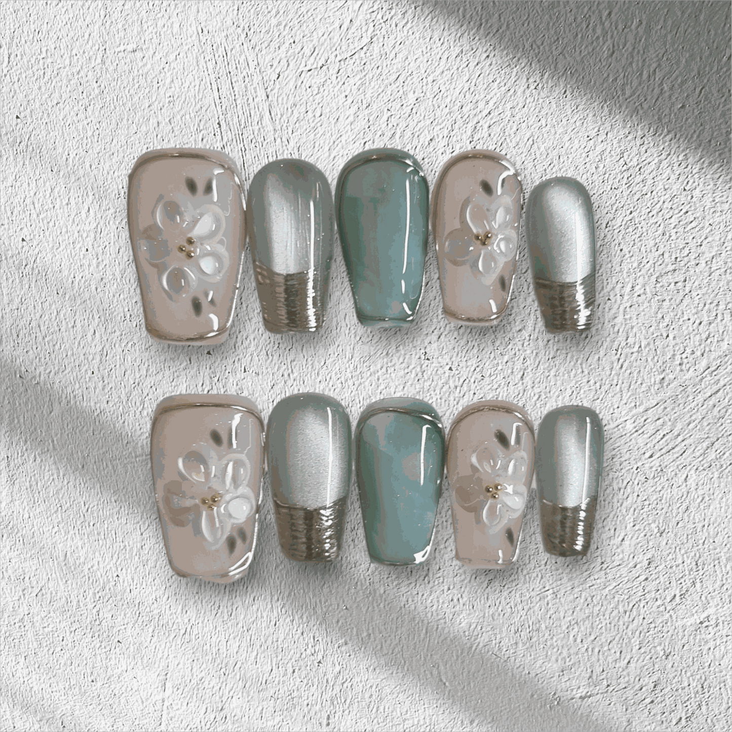 The Glam in GCC press-on nail set in a medium coffin shape, featuring a mix of green, chrome, and 3D floral art nails.