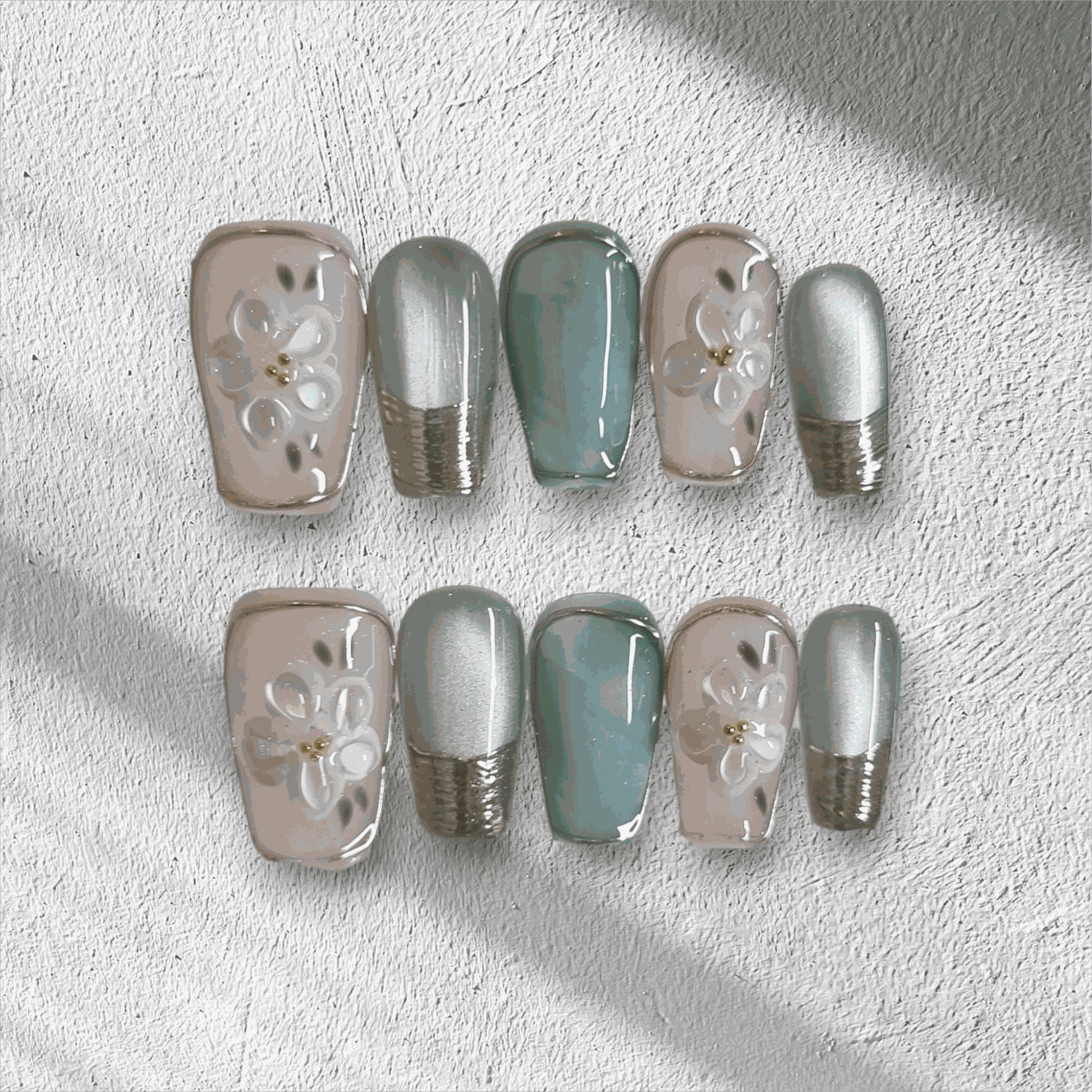 The Glam in GCC press-on nail set in a medium coffin shape, featuring a mix of green, chrome, and 3D floral art nails.