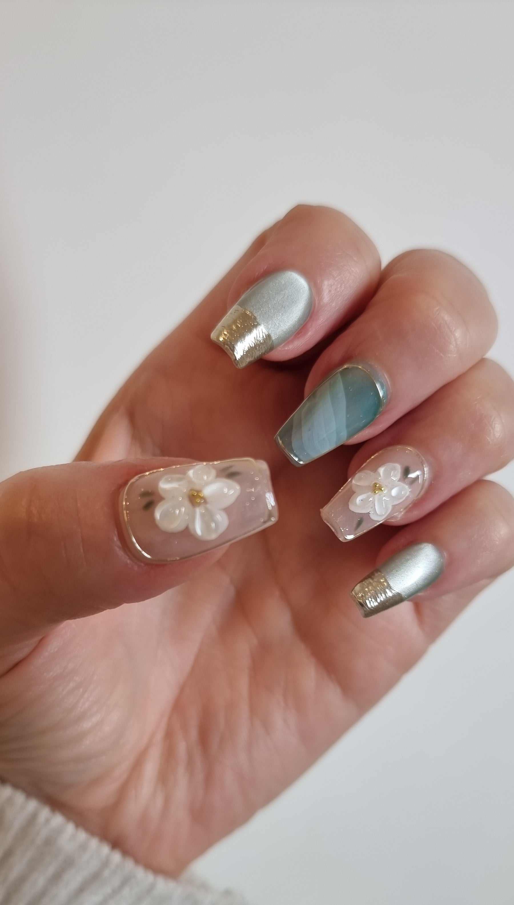 A close-up of the Glam in GCC manicure, highlighting the intricate 3D white floral art and elegant chrome accents.