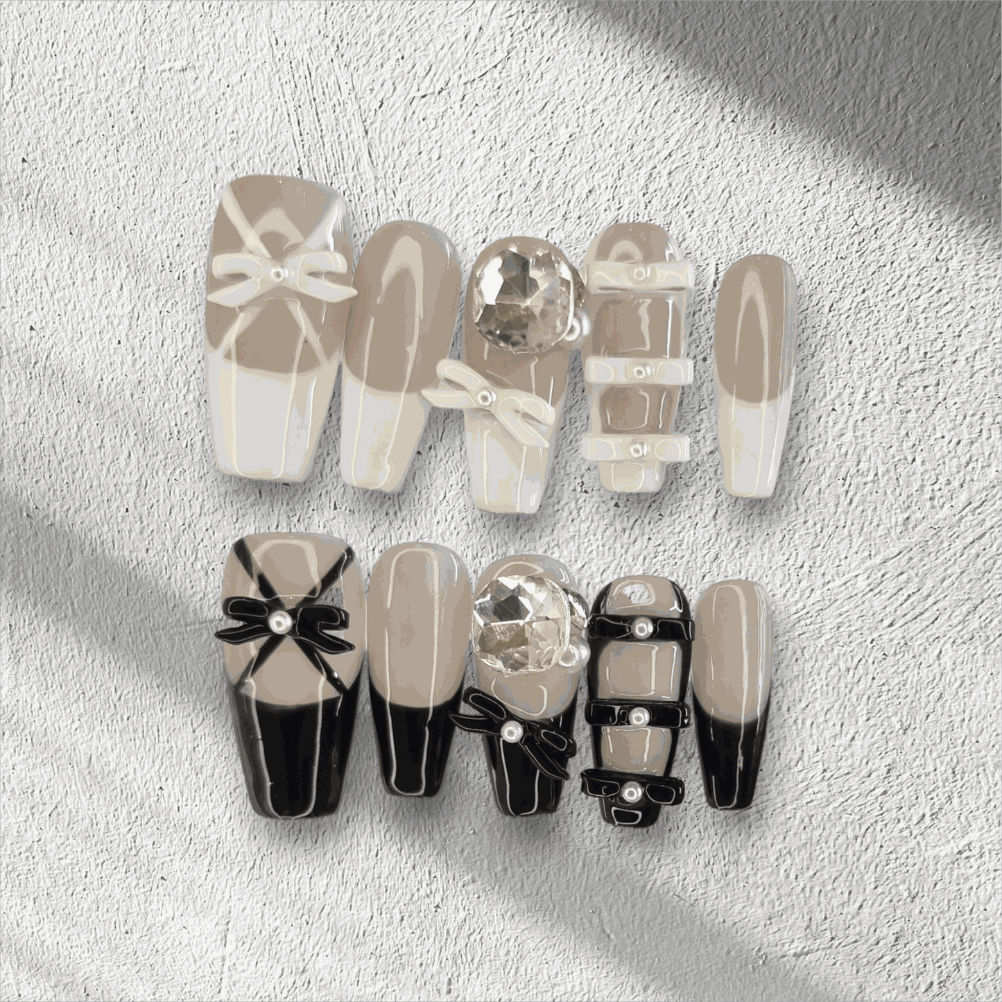 The Hasaas press-on nail set in a long coffin shape, featuring a mix of nude and black nails with large 3D bow and pearl embellishments.