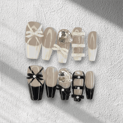 The Hasaas press-on nail set in a long coffin shape, featuring a mix of nude and black nails with large 3D bow and pearl embellishments.