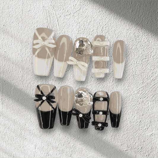 The Hasaas press-on nail set in a long coffin shape, featuring a mix of nude and black nails with large 3D bow and pearl embellishments.