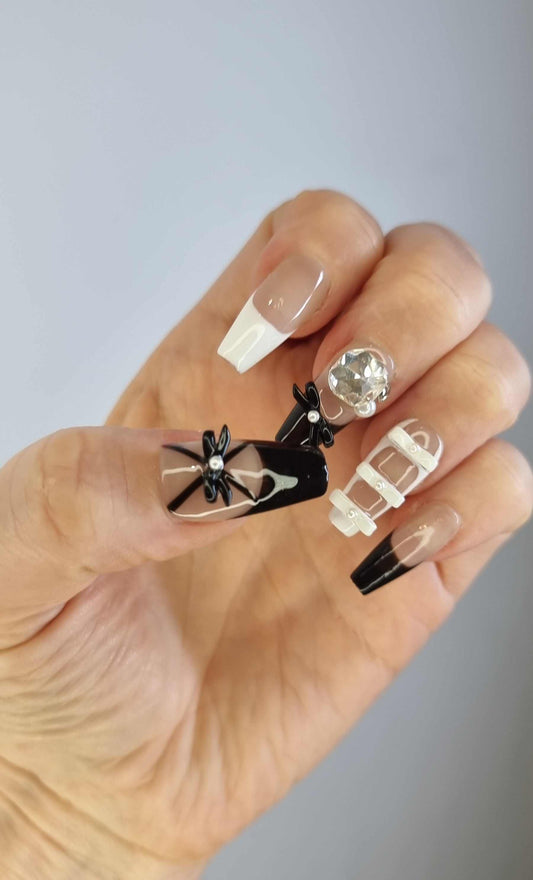 A model's hand showcasing the Hasaas 3D bow press-on nails, highlighting the dramatic black bow and pearl details.