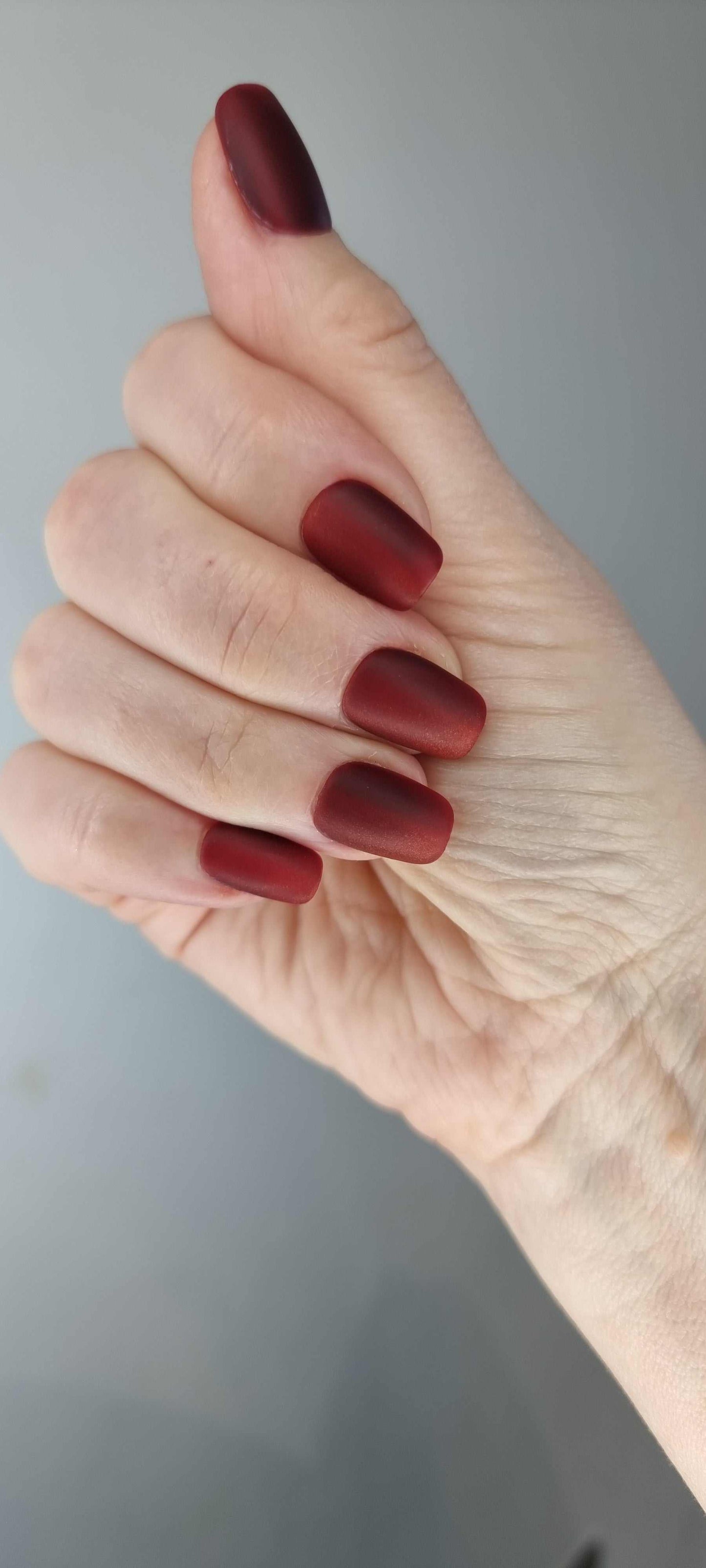 A model's hand wearing the sophisticated Hessa red matte press-on nails, showcasing the elegant square shape.