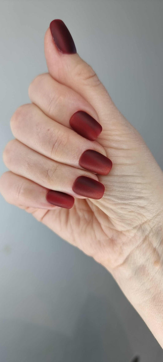 A model's hand wearing the sophisticated Hessa red matte press-on nails, showcasing the elegant square shape.