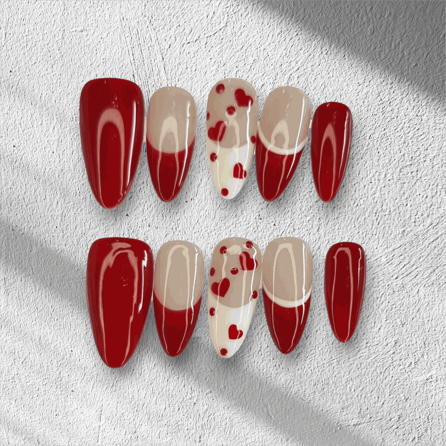 The Holiday Romance press-on nail set in a long almond shape, featuring a mix of solid red, nude, and red heart designs.