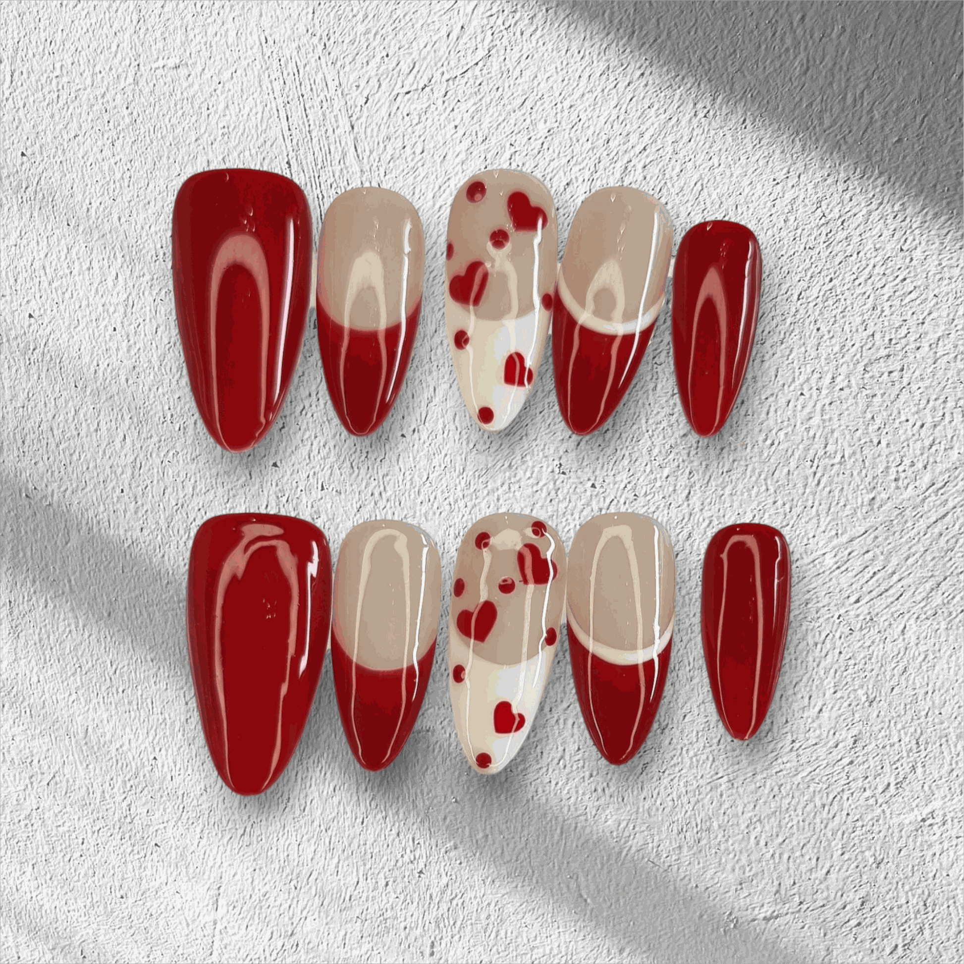 The Holiday Romance press-on nail set in a long almond shape, featuring a mix of solid red, nude, and red heart designs.