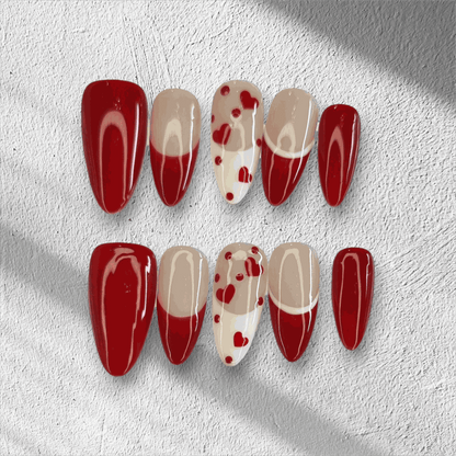 The Holiday Romance press-on nail set in a long almond shape, featuring a mix of solid red, nude, and red heart designs.