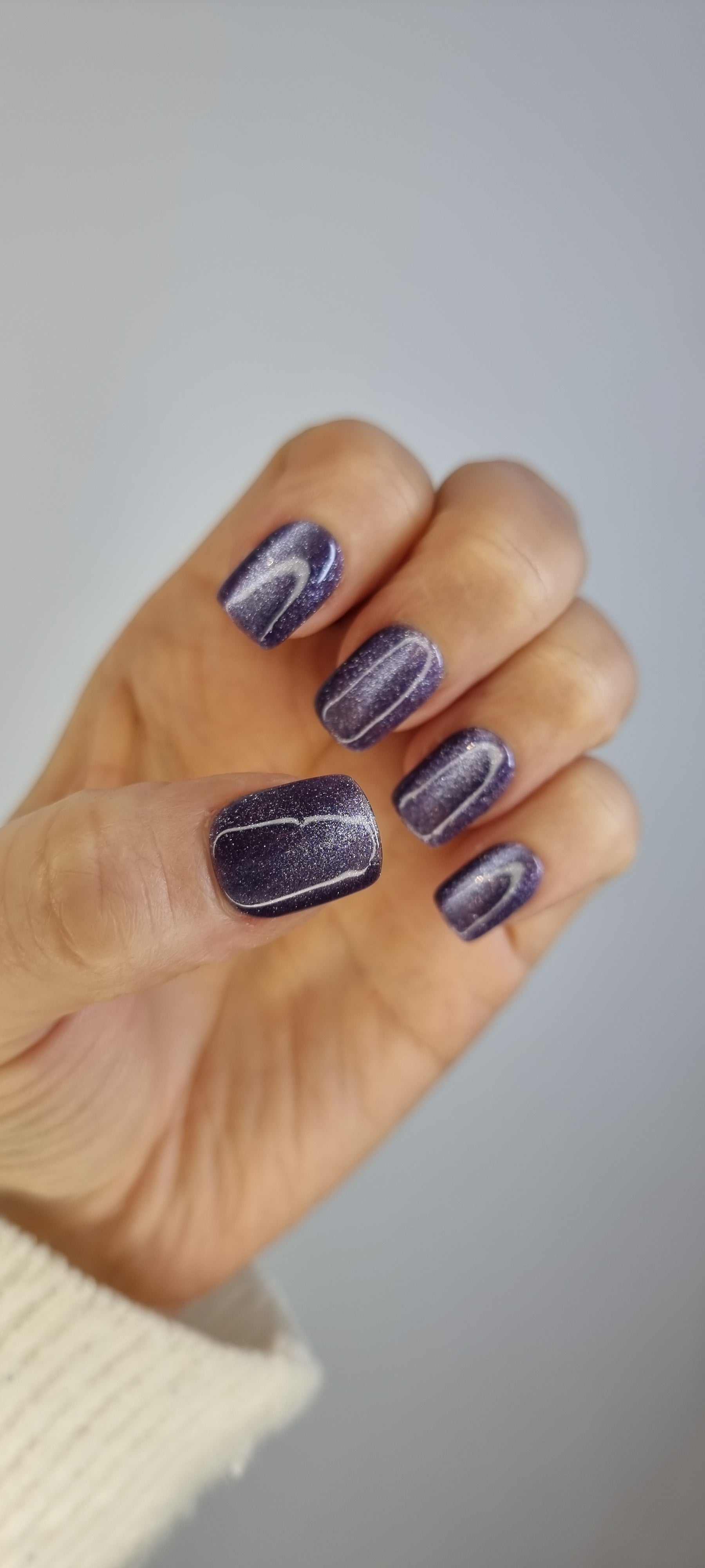 Hand wearing Indigo Rain short square press-on nails in a dark gray color with a glossy, shimmering finish.