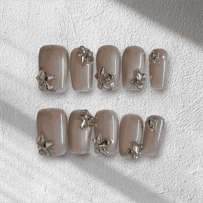 Jeddah Glow pearlescent nude short square press-on nails by Nail Addict, featuring shiny silver 3D flower and leaf accents.