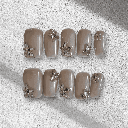 Jeddah Glow pearlescent nude short square press-on nails by Nail Addict, featuring shiny silver 3D flower and leaf accents.