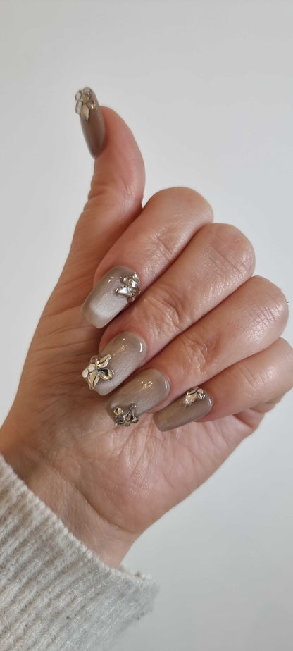 Hand wearing Jeddah Glow short square press-on nails with a glossy pearlescent finish and intricate 3D silver flower details.