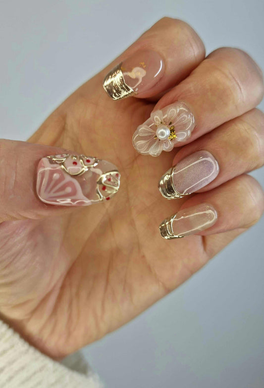 Hand wearing Jenny long coffin press-on nails with a variety of designs, including a 3D flower, gold foil, and white and pink swirls.