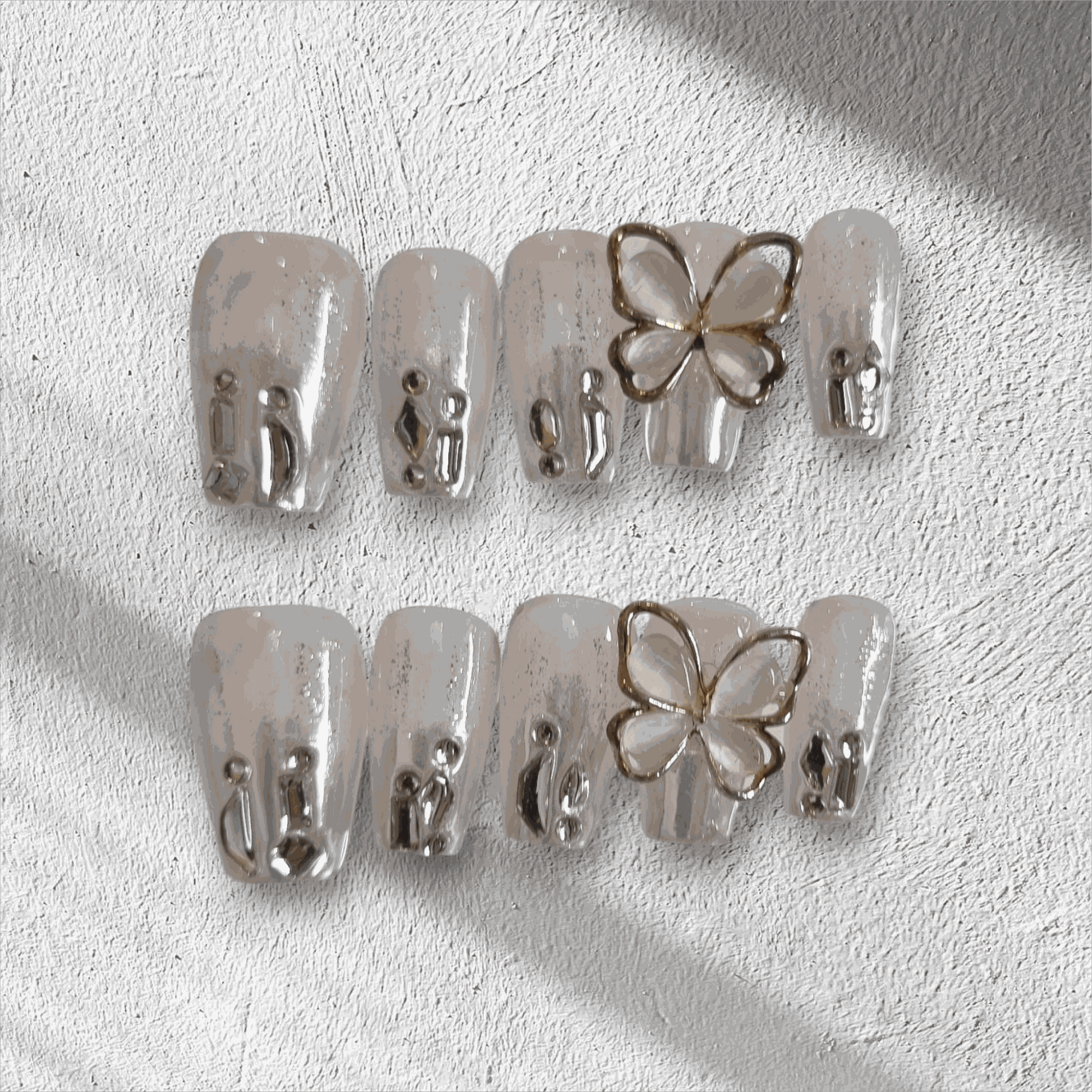 Jessie nude glitter coffin press-on nails by Nail Addict, featuring silver liquid-effect accents and a 3D butterfly charm.