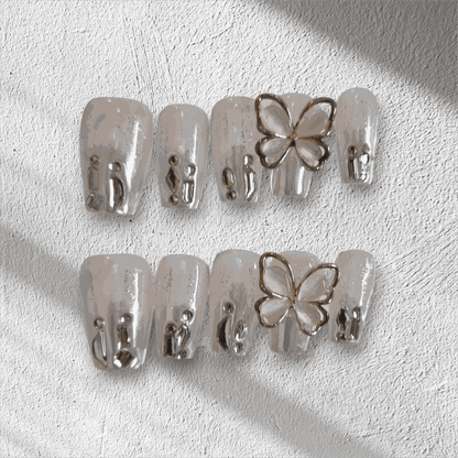 Jessie nude glitter coffin press-on nails by Nail Addict, featuring silver liquid-effect accents and a 3D butterfly charm.