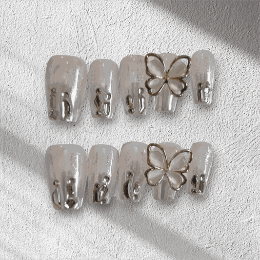 Jessie nude glitter coffin press-on nails by Nail Addict, featuring silver liquid-effect accents and a 3D butterfly charm.