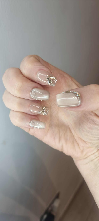 Hand wearing Joud long square press-on nails in a nude shade with a glossy finish and silver chrome accents.