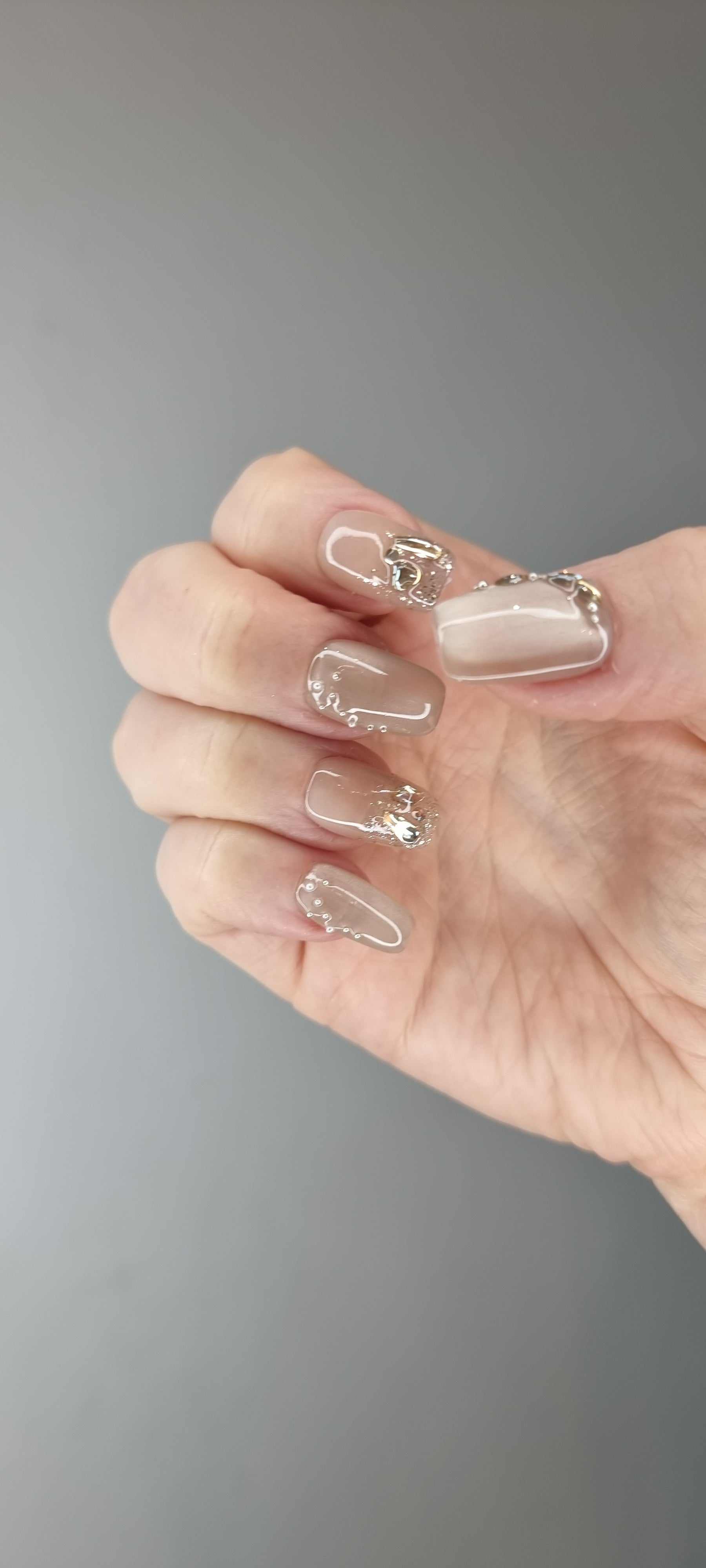Hand wearing Joud short square press-on nails in a nude shade with a glossy finish and silver chrome accents.