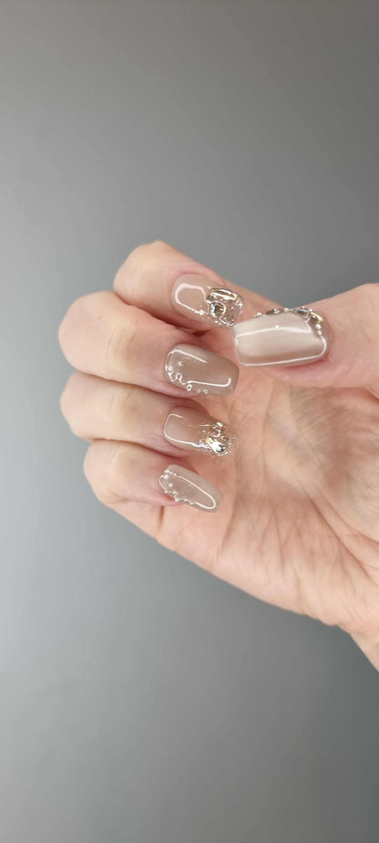 Hand wearing Joud short square press-on nails in a nude shade with a glossy finish and silver chrome accents.