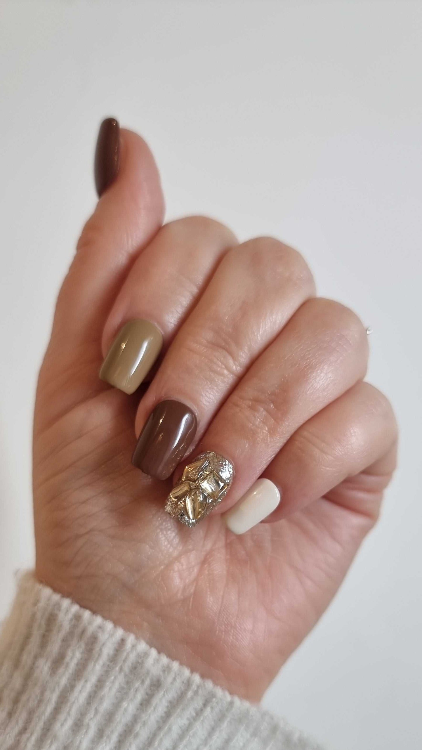 Hand wearing Jumeirah Glow short square press-on nails by Nail Addict, showcasing the polished brown and nude shades and the glamorous gold accent.