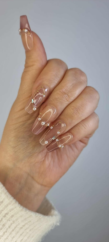 Hand wearing Khawla long coffin press-on nails in brown and nude, with detailed gold chain and pearl embellishments.