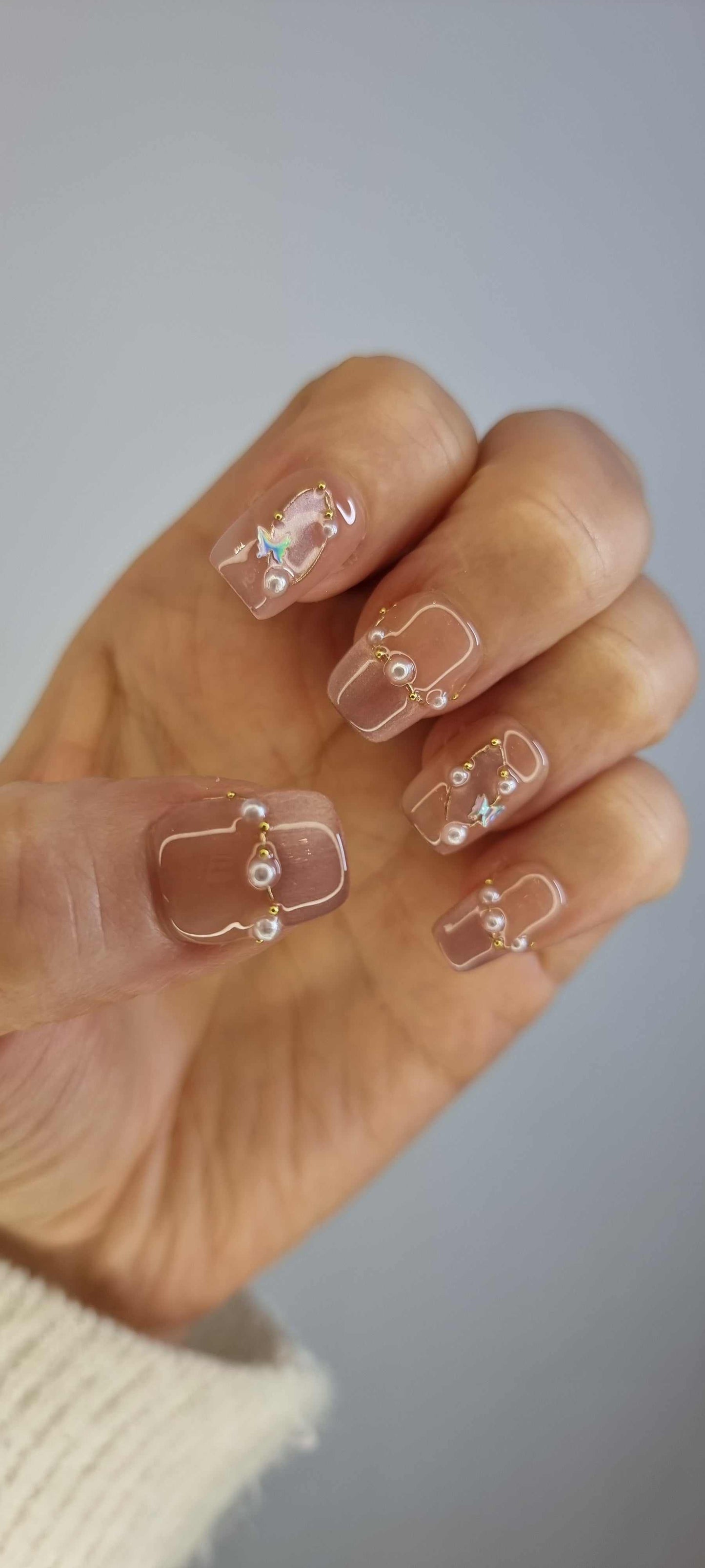  Hand wearing Khawla brown and nude press-on nails by Nail Addict, featuring elegant gold chains and pearl accents on each nail.